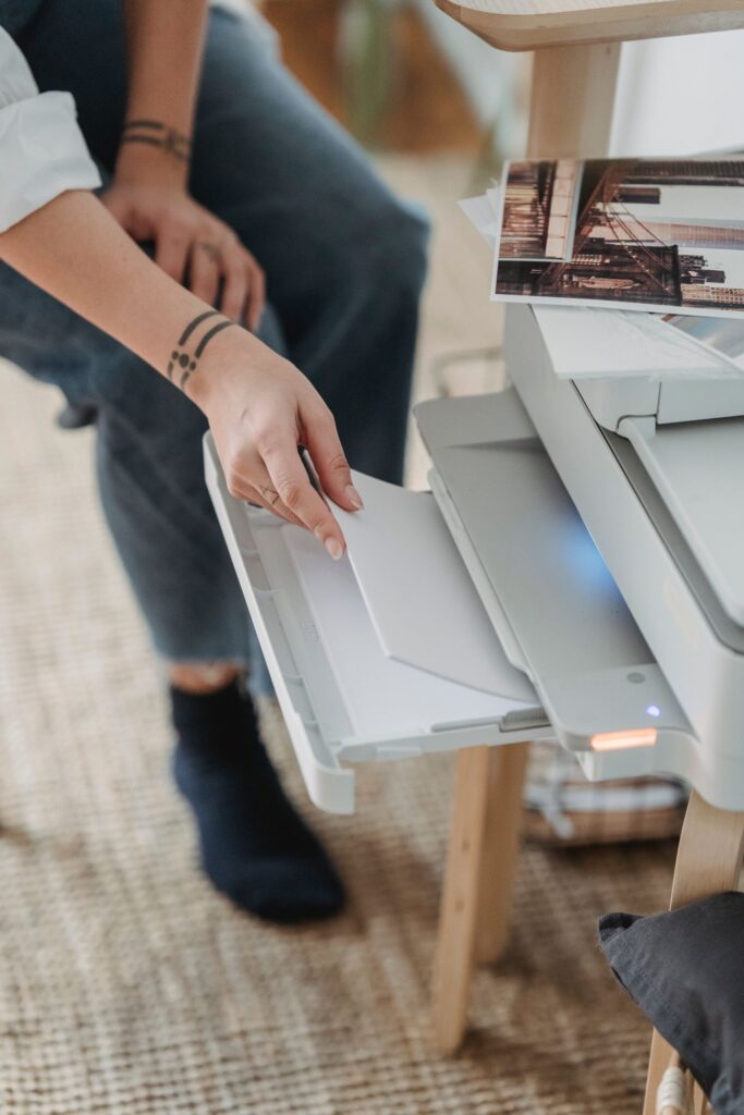 Person handling paper in a home printer beside printed photos; IRCC web form guide.